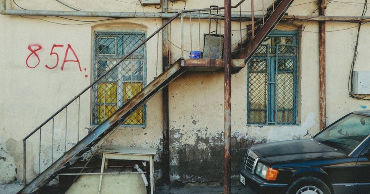 Rustic building facade with stairway, windows, and an old car parked outside.