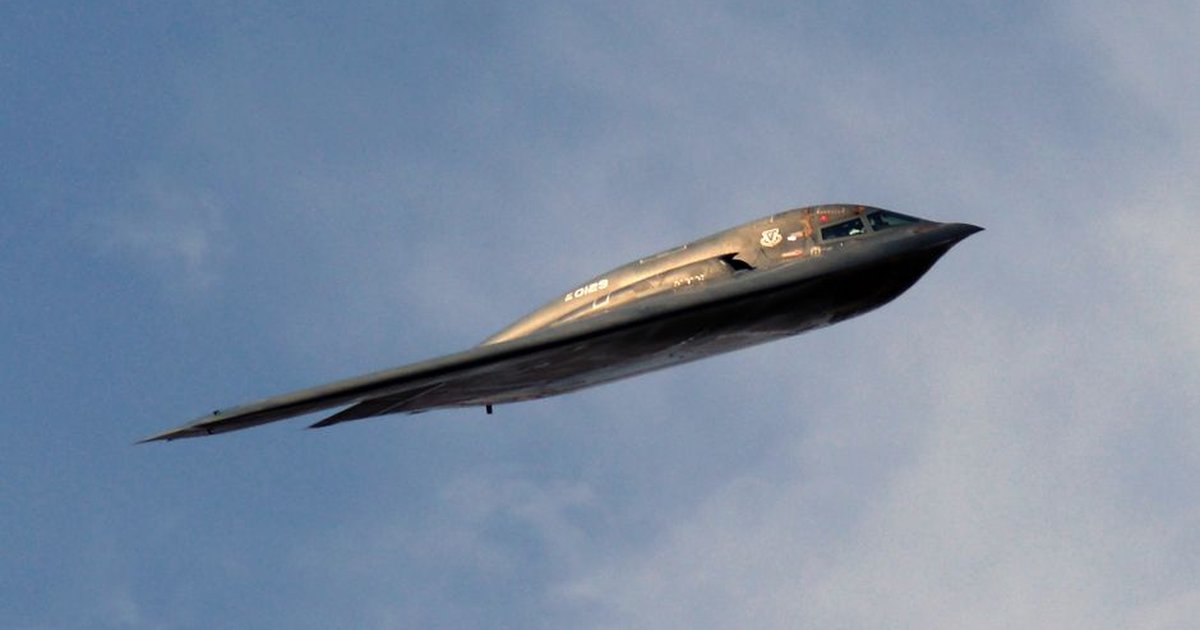 A stealth bomber aircraft soaring smoothly through a clear blue sky during the day.