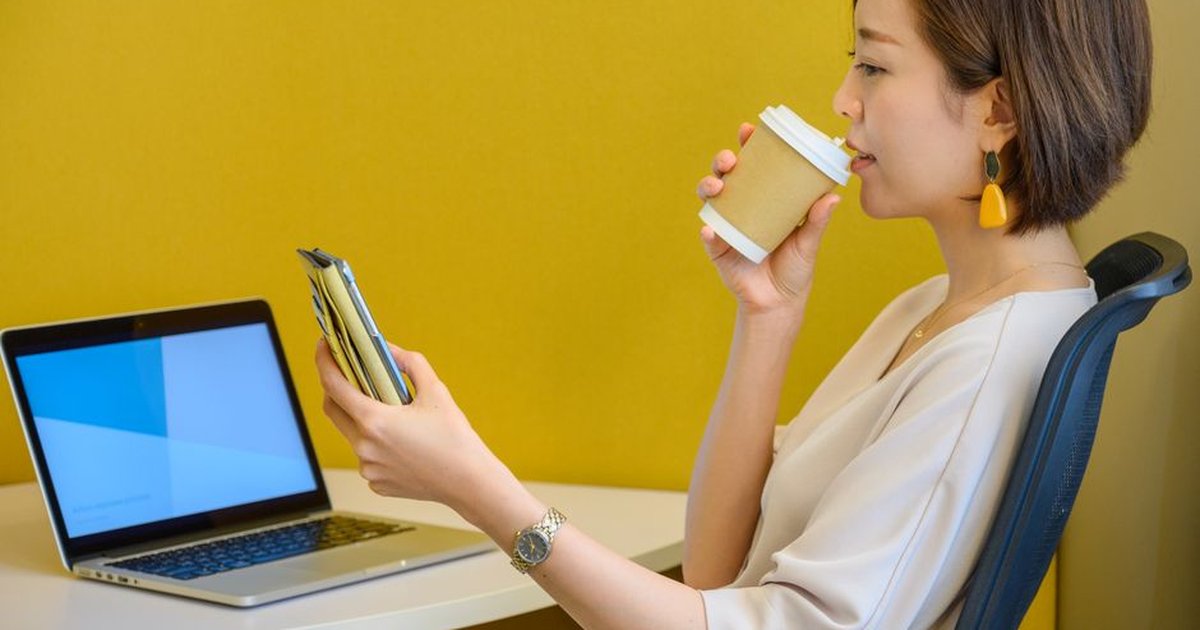 Young woman multitasking with smartphone and coffee at workstation.