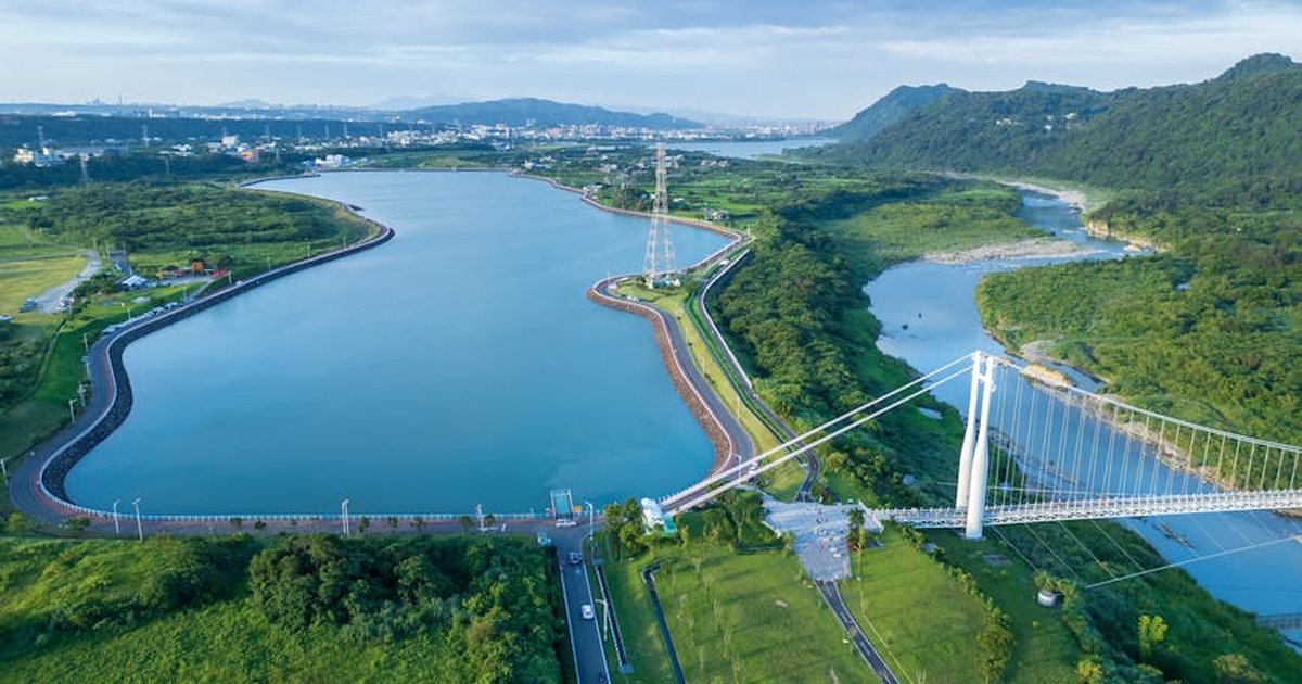 Aerial view of a scenic river winding through lush green landscape with a modern suspension bridge.
