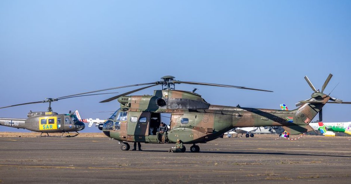 Military helicopters with crew members preparing on a runway under clear sky.