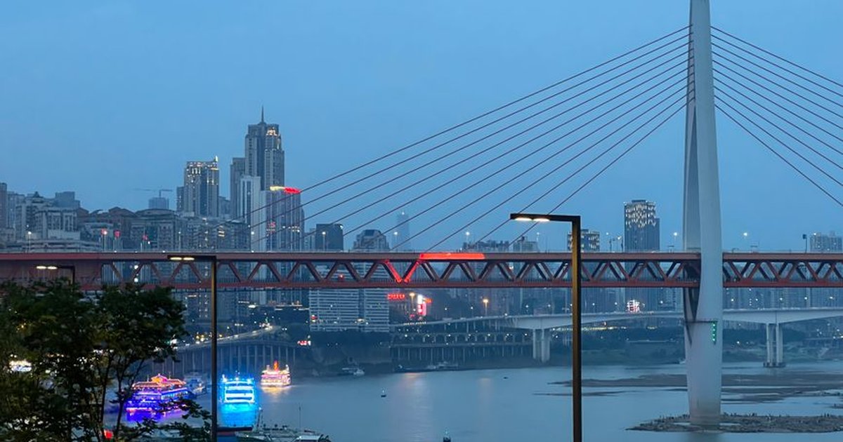 Aerial view of Chongqing at dusk with Qiansimen Bridge and illuminated skyline.