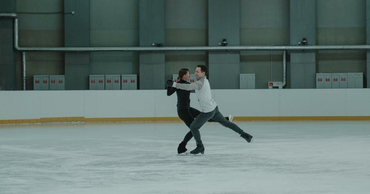 Two athletes gracefully perform a figure skating routine on an indoor rink.