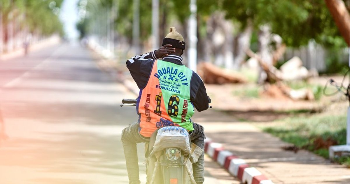 Back view of a motorcyclist riding along a sunny road in Douala, Cameroon.