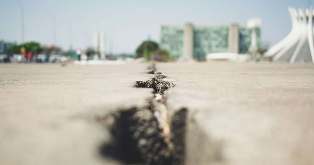 Close-up of a cracked pavement with buildings in the blurred background, emphasizing urban decay.