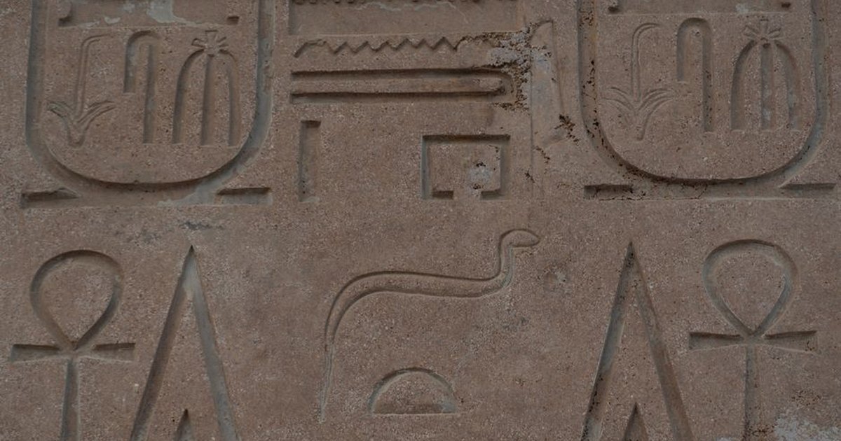 Close-up of ancient Egyptian hieroglyphs carved on a sandstone wall, showing iconic symbols and inscriptions.