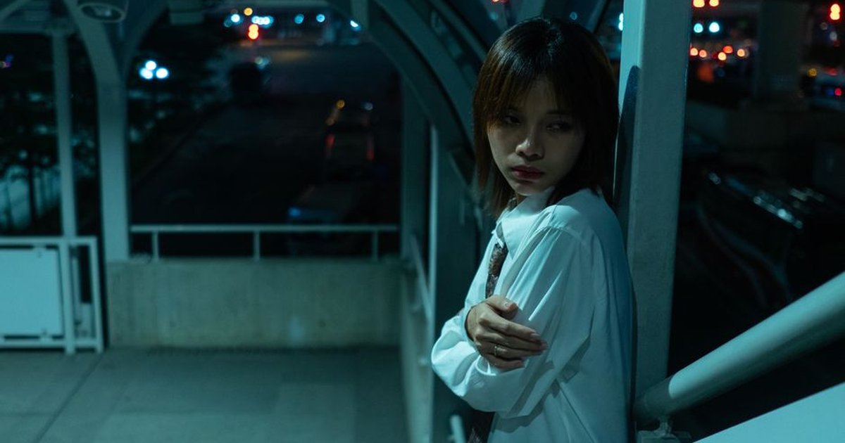 A contemplative young woman stands in an urban walkway at night, evoking a moody atmosphere.