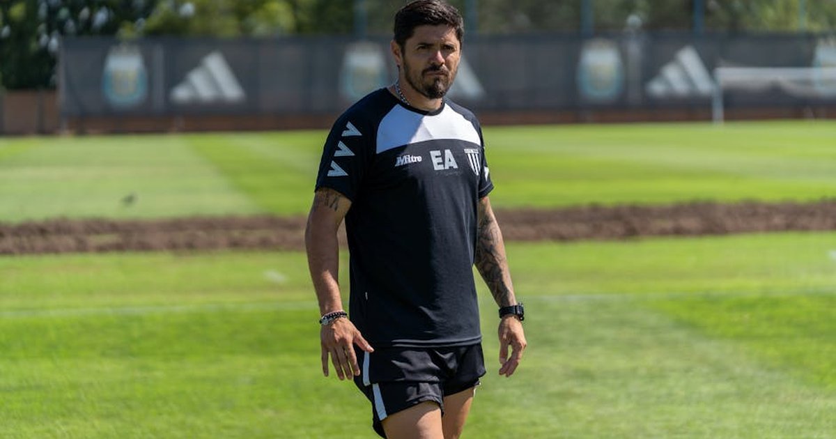 A sports coach walks confidently on a sunny training field.