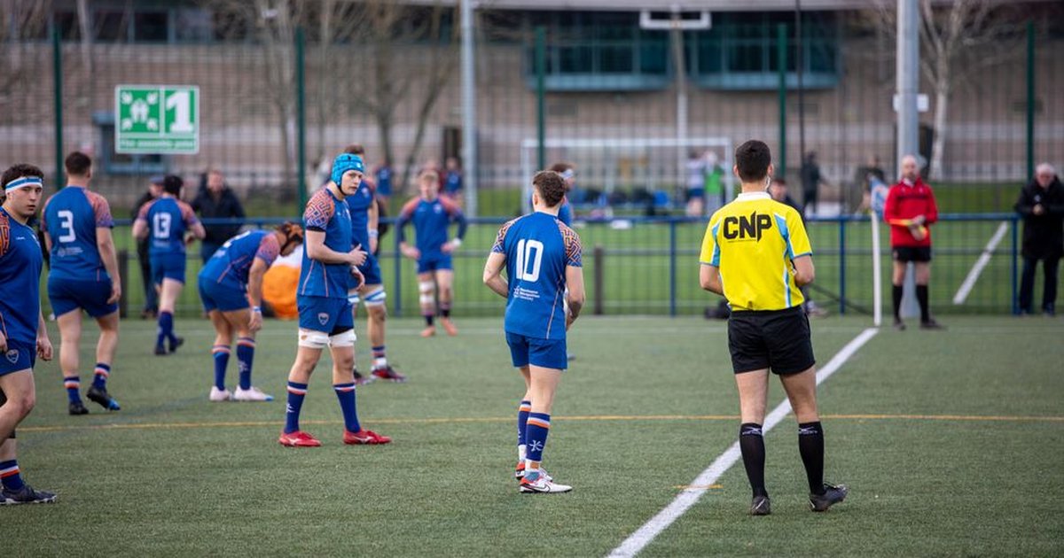 Action-packed rugby match with teams in blue and referee in a stadium, Manchester, UK.