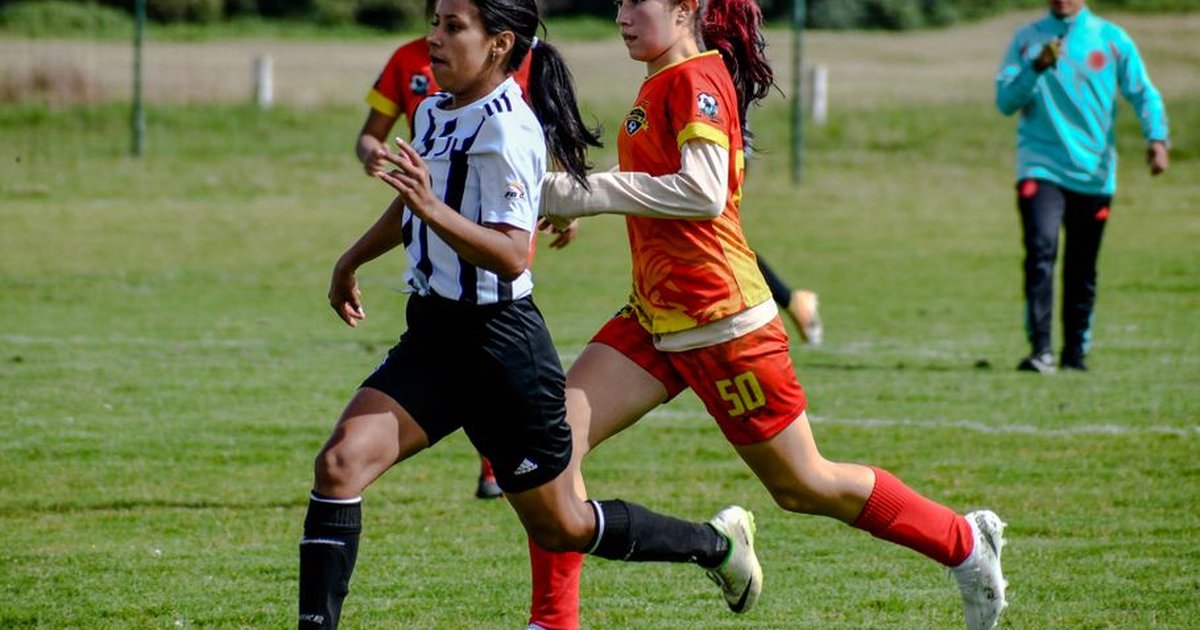 Two young women competing in a soccer match on a sunny day. Action, sports, and teamwork depicted.