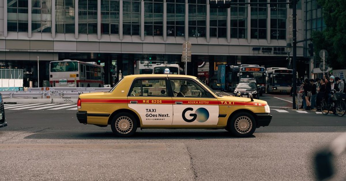 A traditional yellow taxi in an urban setting during the day, showcasing traffic and city life.