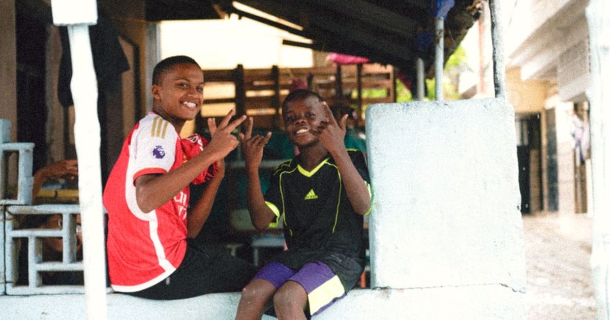 Two smiling children sitting outdoors, showing playful gestures, embodying friendship and fun.