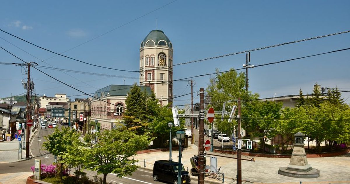 Historic clock tower in a lively urban setting with clear skies and lush greenery.