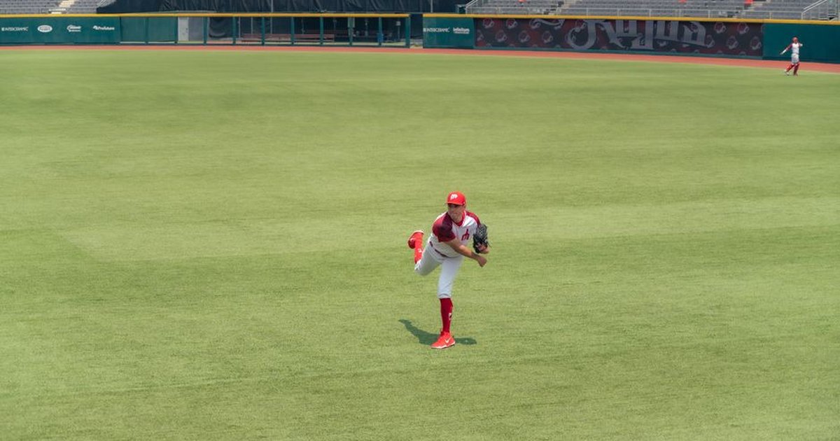 A baseball player pitching on a grass field in an empty stadium.