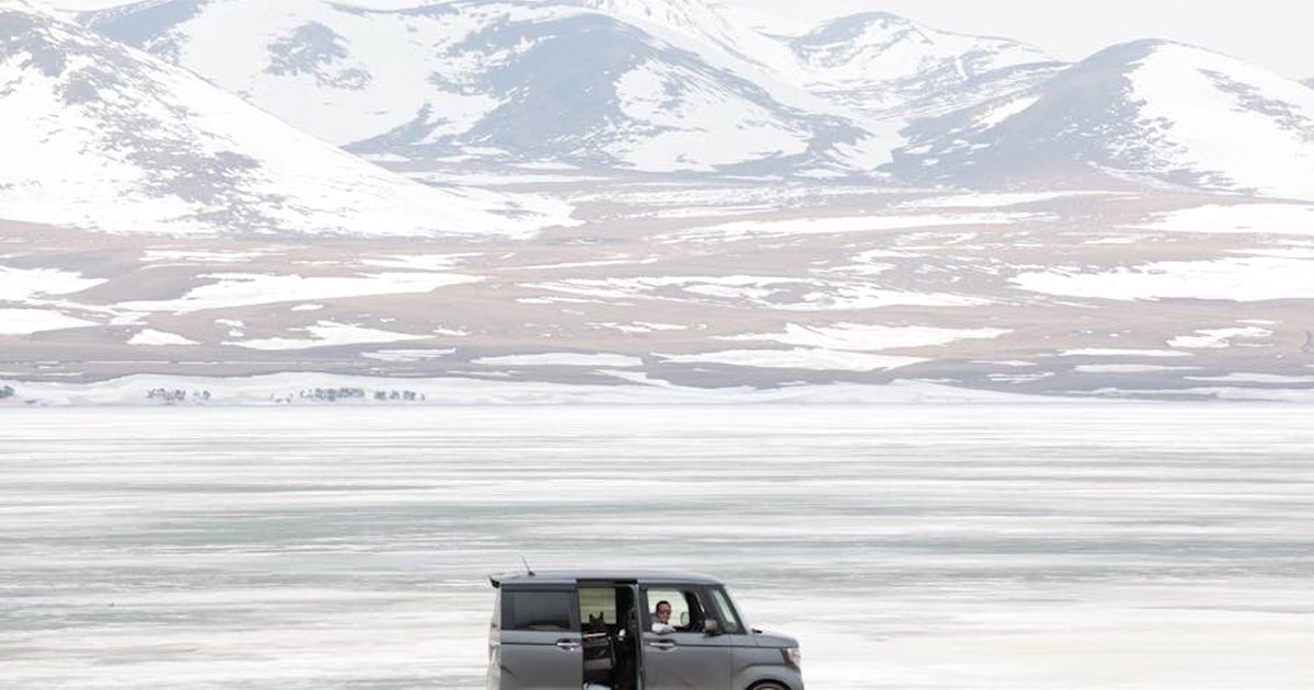 A van parked by a frozen lake against a backdrop of snow-covered mountains, perfect for winter adventures.