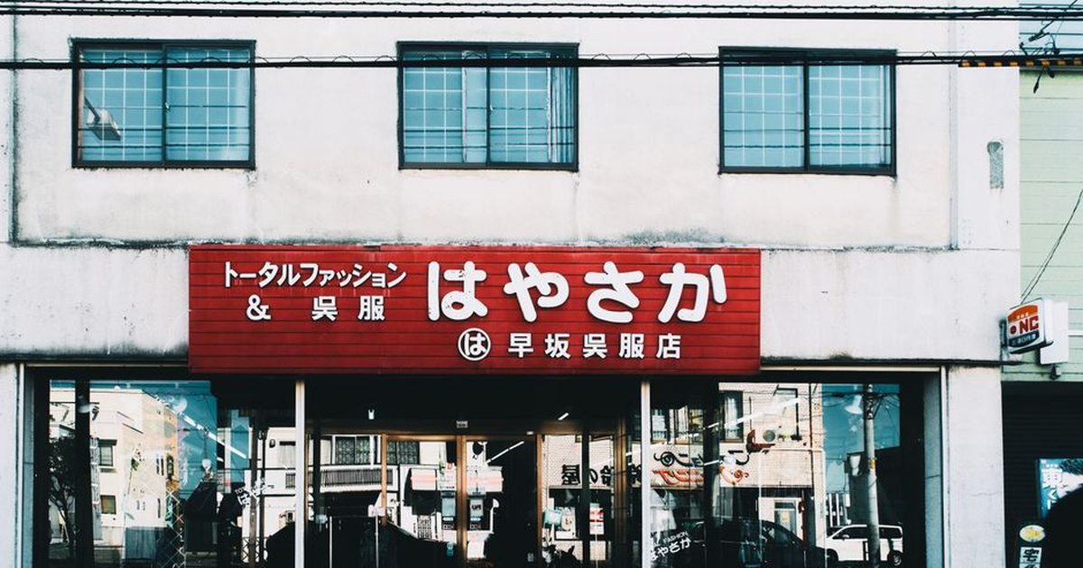Street view of a Japanese clothing shop with a prominent red sign and glass windows.