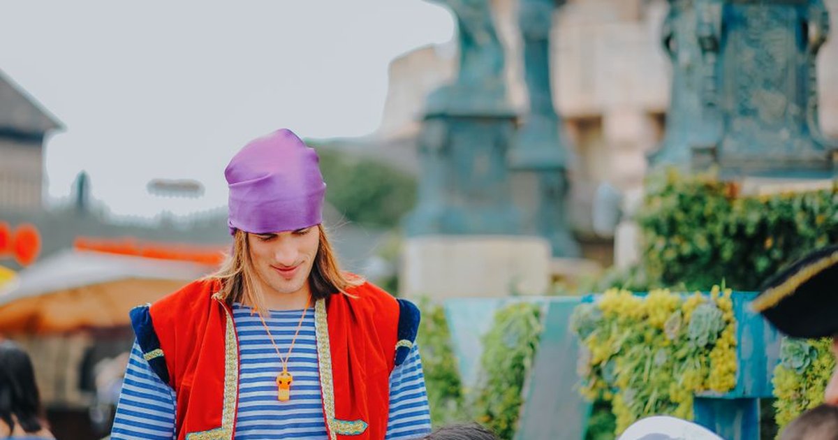 A person wearing a vibrant costume with a purple bandana enjoys an outdoor event.