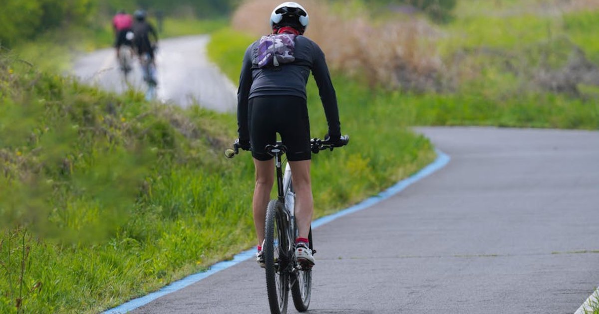 A cyclist enjoying a ride on a winding countryside road, surrounded by green nature.
