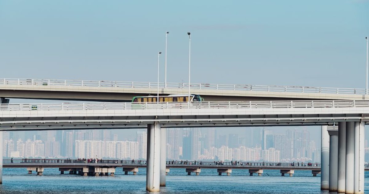 A contemporary bridge stretching over water with a city skyline in the distance.