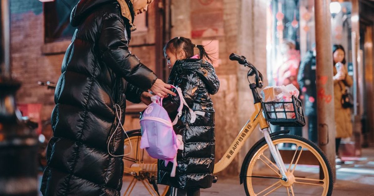 A mother helping her daughter with a backpack on a vibrant Beijing street at night.