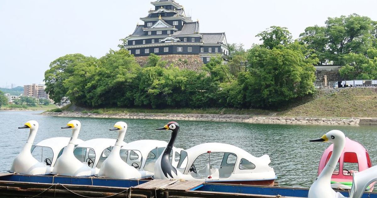 Swan-shaped boats on Asahi River with Okayama Castle in the background, Japan.
