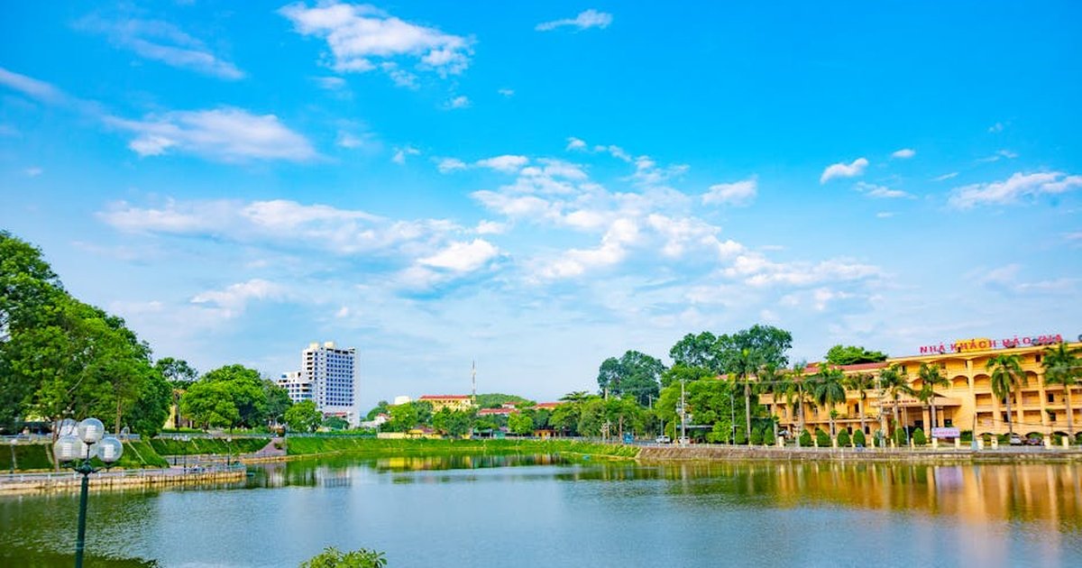 A serene urban landscape featuring a lake and city buildings under a bright blue sky.