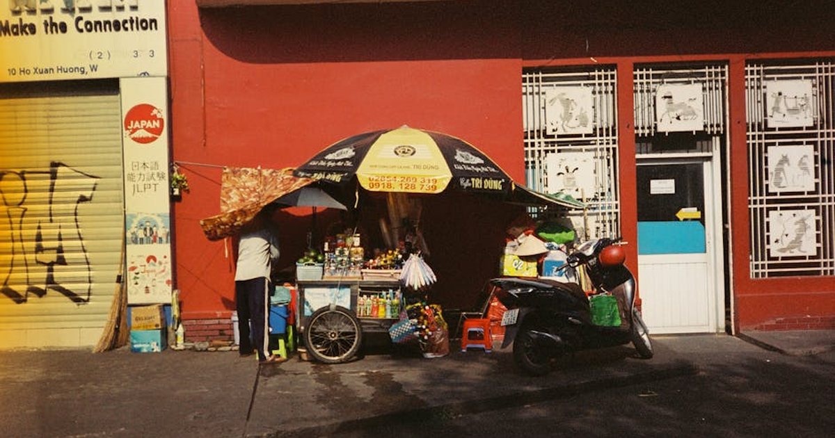 Colorful street vendor stall against a red wall with a scooter parked nearby.