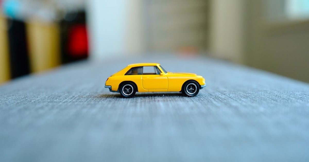 Close-up of a small yellow toy car placed on a table indoors, showcasing minimal design.