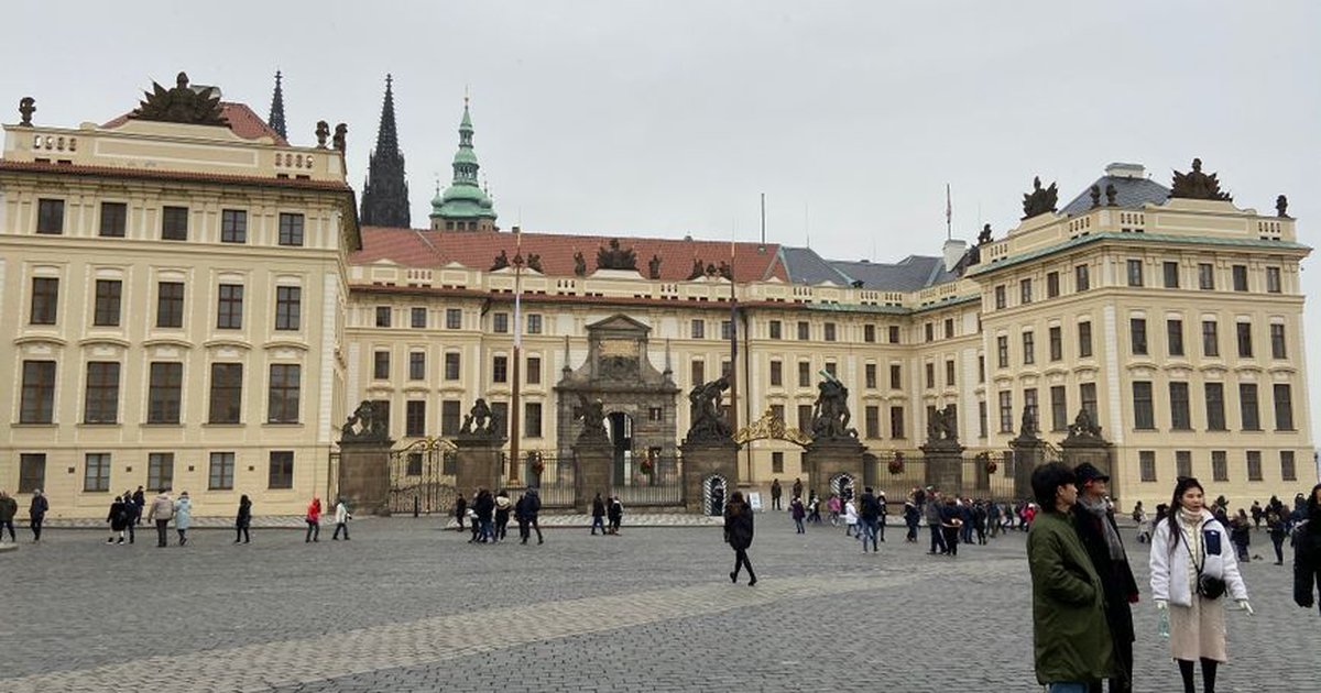 Tourists explore Prague Castle's grand facade under a gray, cloudy sky.