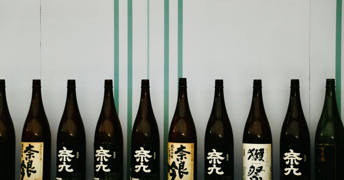 A row of Japanese sake bottles displayed on a wooden shelf against a decorative backdrop.
