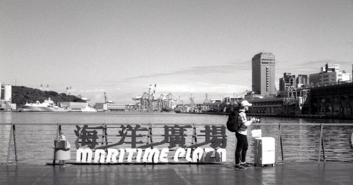 Monochrome photo of Maritime Plaza in Taipei, featuring a man near the waterfront with city skyline and ships.