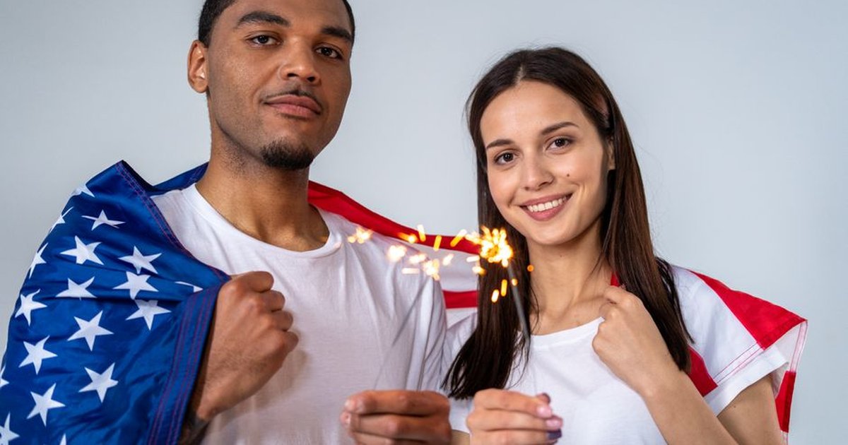 Couple celebrates Independence Day with a sparkler and American flag.