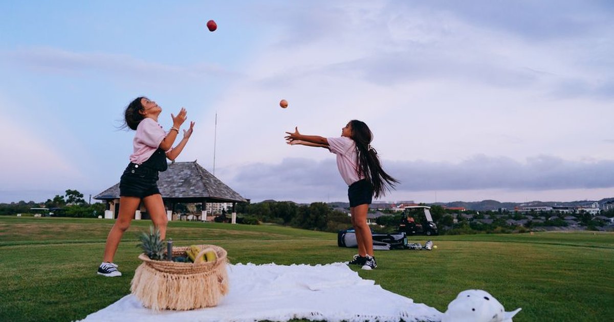 Two girls enjoy an outdoor picnic, playing and juggling apples on a sunny day.