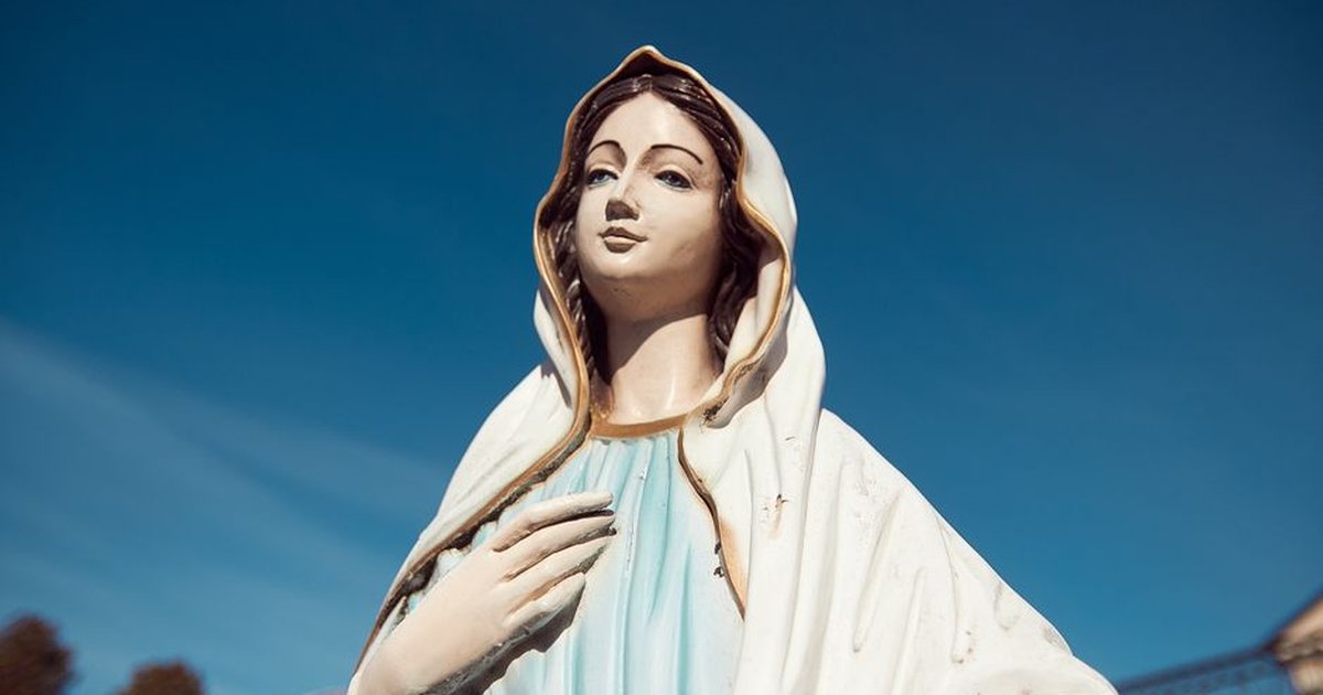 A serene statue of the Virgin Mary stands against a clear blue sky, symbolizing peace and faith.