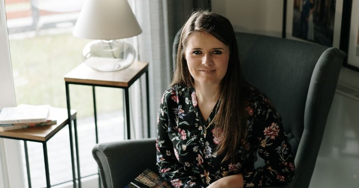 Brunette woman sitting comfortably in an armchair, enjoying a book in a cozy, well-lit living room.