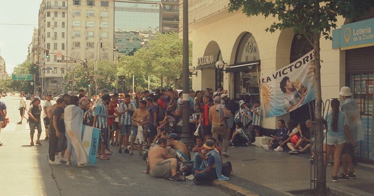 Lively crowd gathers on a bustling street in Buenos Aires, celebrating with flags and banners.
