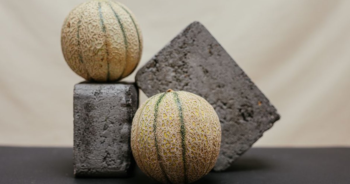 A creative studio shot featuring cantaloupe melons artistically arranged with geometric concrete blocks.