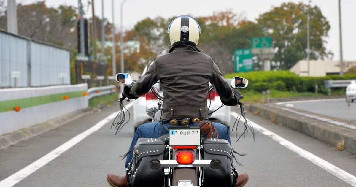 A motorcyclist in a leather jacket rides on a highway in Japan, showcasing road travel spirit.