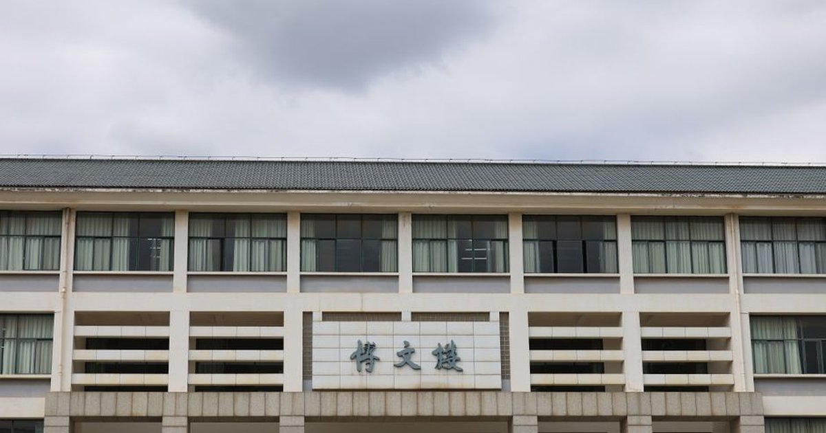 Front view of a modern educational building with Asian architectural elements under a cloudy sky.