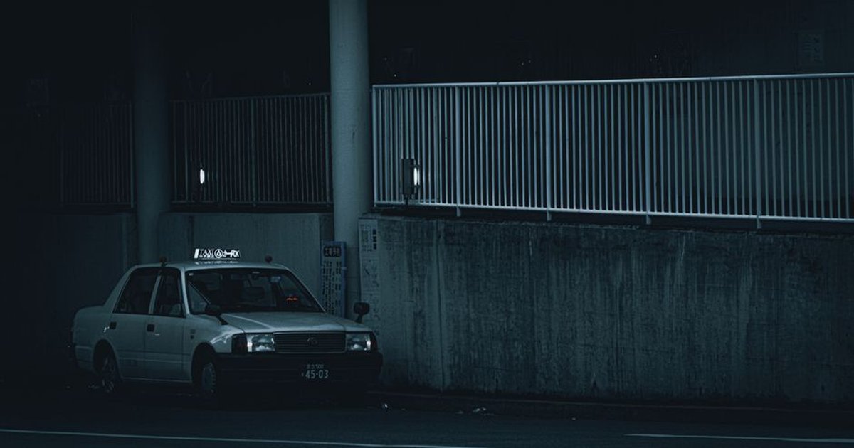 A lonesome taxi parked under a dimly lit urban area at night.