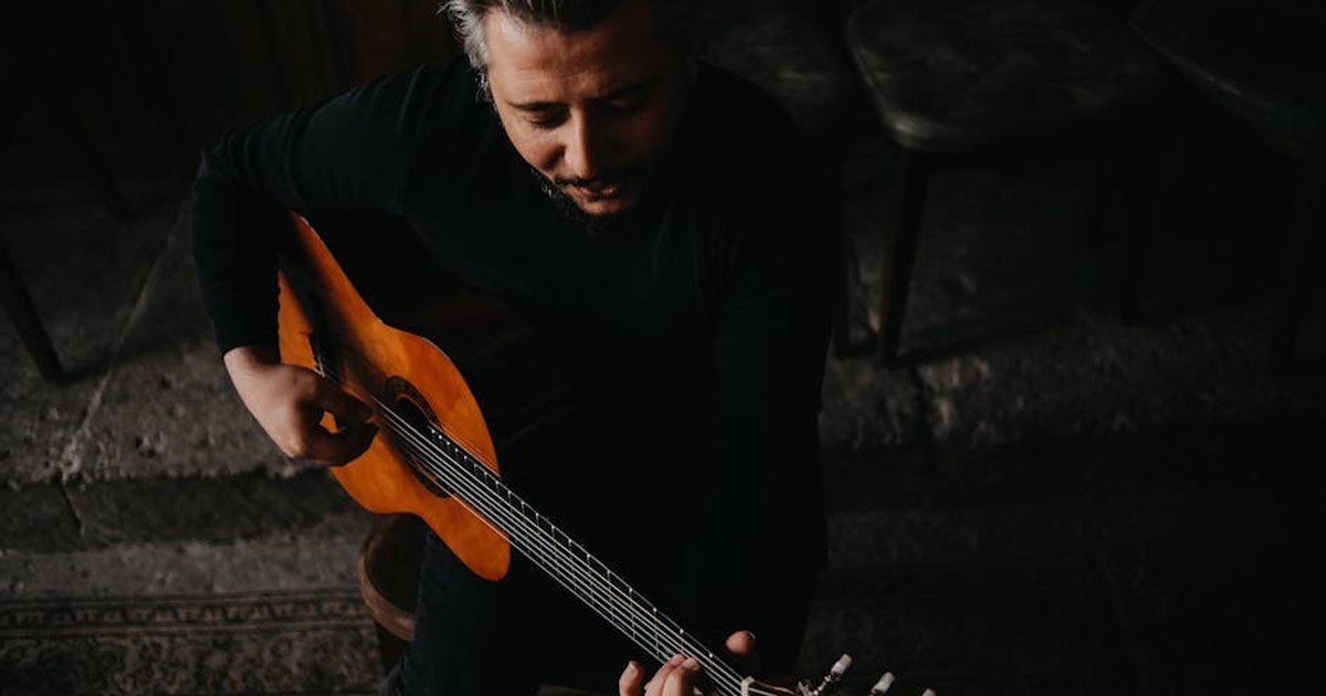 Male musician playing acoustic guitar, captured in a moody and artistic setting.