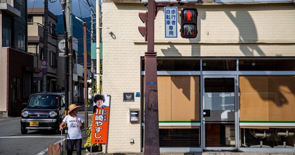 Street view in Nagano City, featuring a person waiting at a crosswalk under a traffic light.