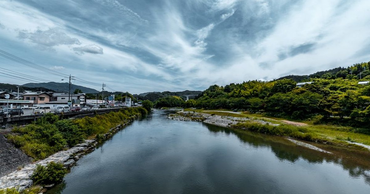 Peaceful river with lush green banks under a dramatic sky, perfect for nature lovers.