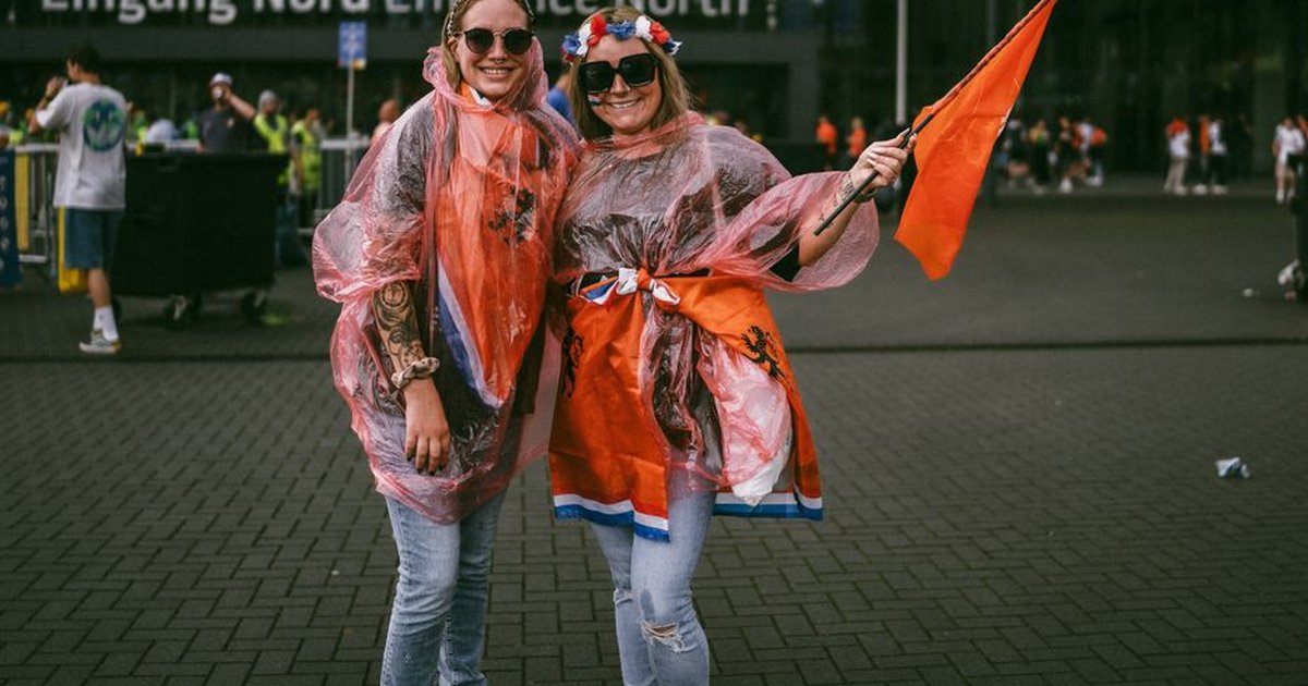 Two joyful soccer fans in raincoats and flags at a stadium entrance, enjoying a vibrant event.