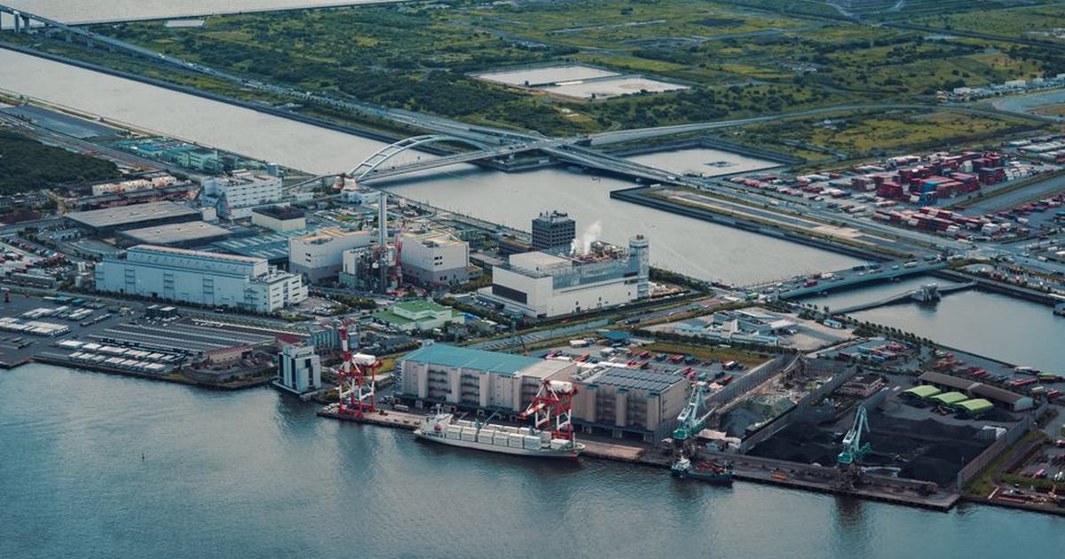 Aerial view of Tokyo's industrial port by the water, featuring cranes and containers.