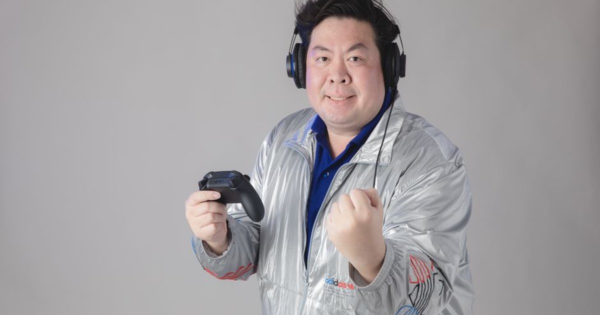 Asian man with headphones celebrates while gaming, holding a controller.