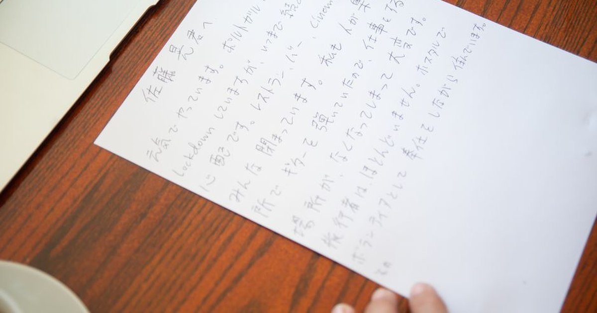 Close-up of a handwritten Japanese letter on a wooden desk with a laptop and tea cup.