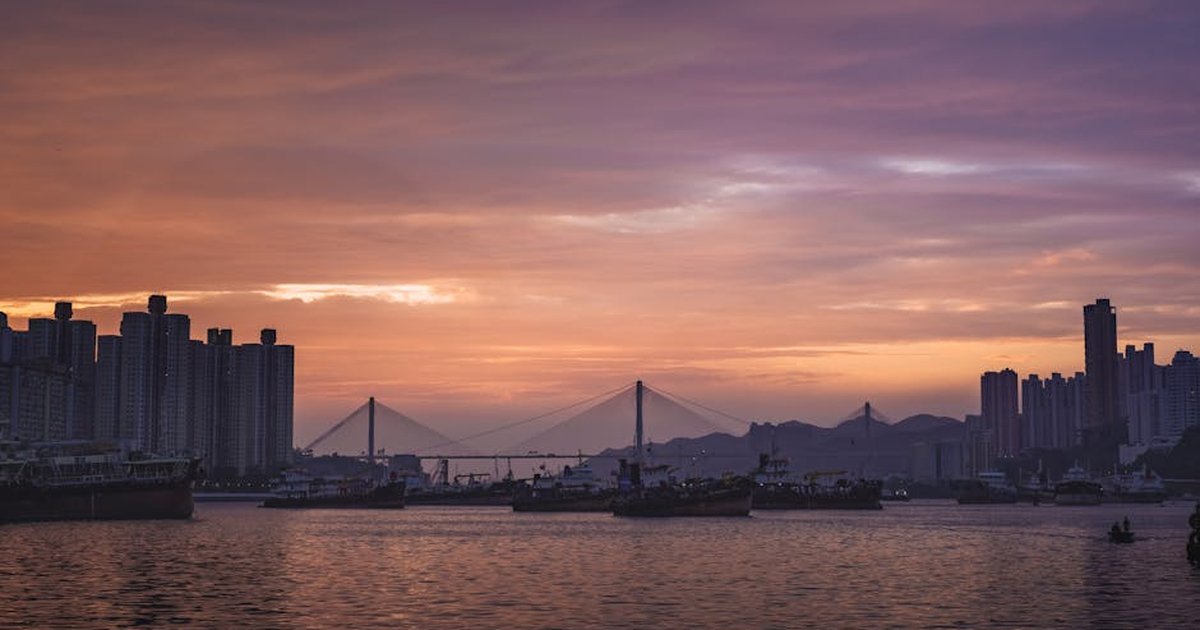 Serene view of Hong Kong's skyline and bridge at twilight, showcasing stunning colors and reflections.