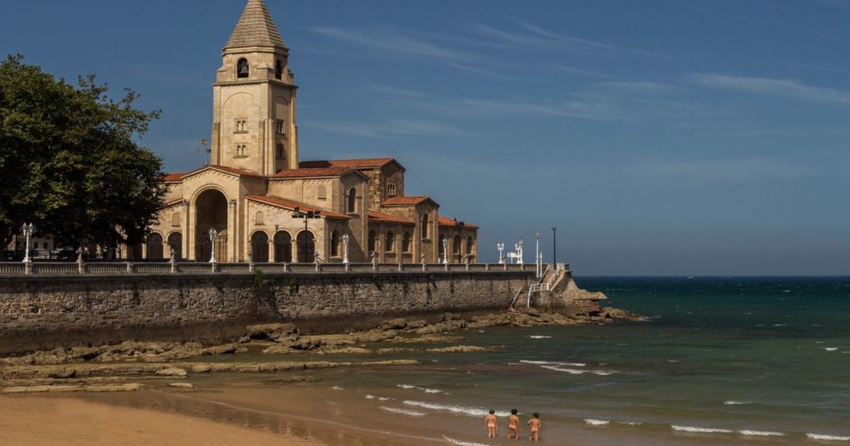 Charming coastal church next to a beach with people in the sea.