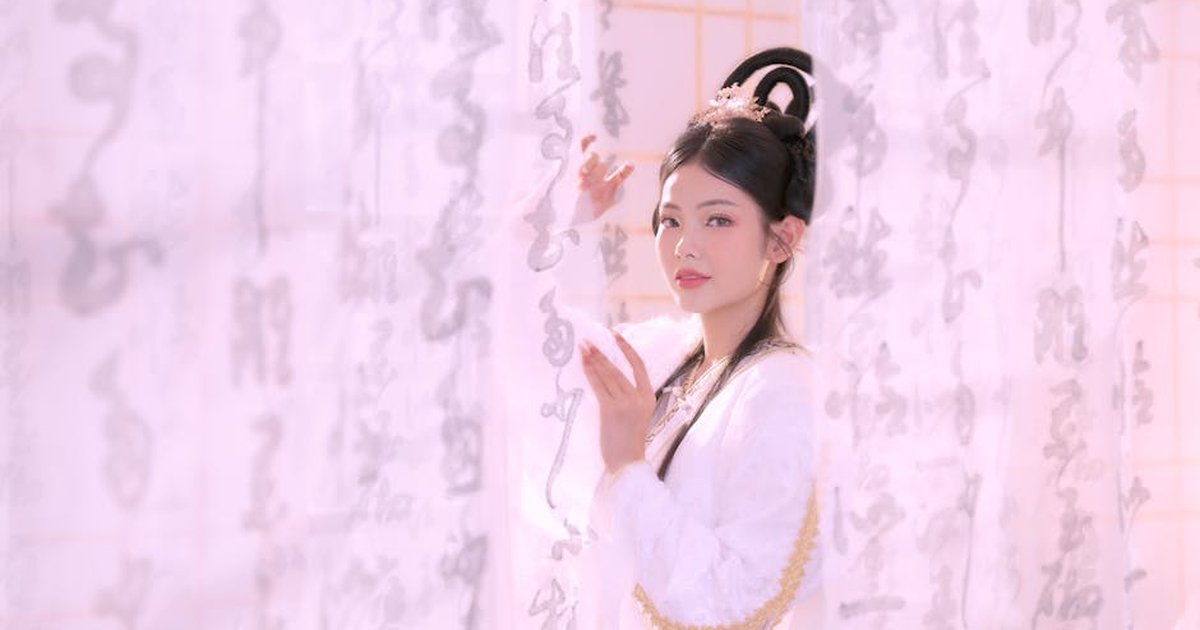 A young woman in traditional attire poses elegantly behind sheer curtains with calligraphy.